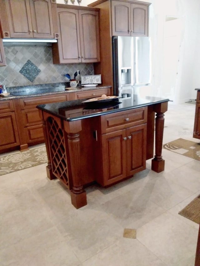 kitchen with refrigerator with ice dispenser, dark countertops, a kitchen island, black electric stovetop, and backsplash