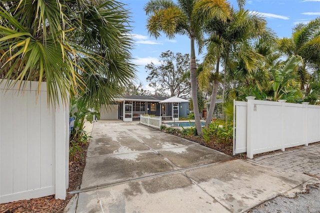 exterior space with driveway, a sunroom, a fenced in pool, and fence