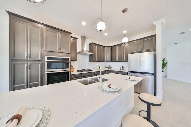 kitchen featuring a sink, pendant lighting, dark brown cabinetry, appliances with stainless steel finishes, and wall chimney exhaust hood