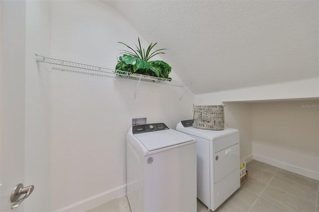 clothes washing area with a textured ceiling, baseboards, laundry area, washer and dryer, and light tile patterned floors