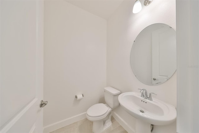 half bath featuring baseboards, toilet, tile patterned flooring, and a sink
