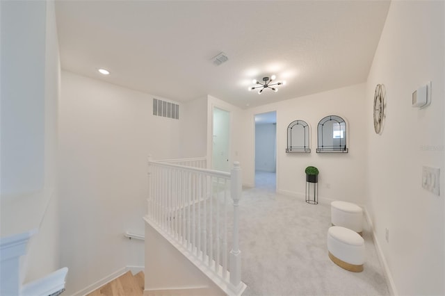 hall with baseboards, an upstairs landing, visible vents, and light carpet