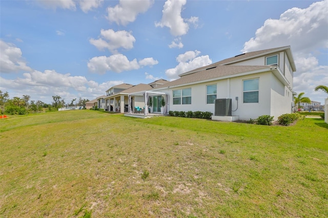 rear view of property featuring central AC unit, a shingled roof, stucco siding, and a yard