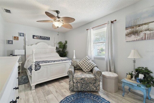 bedroom featuring light wood-style flooring, visible vents, a textured ceiling, and a ceiling fan