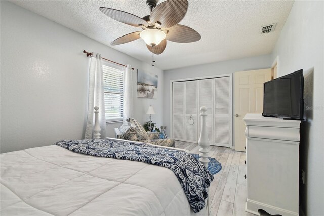bedroom featuring a textured ceiling, visible vents, light wood-style floors, a ceiling fan, and a closet