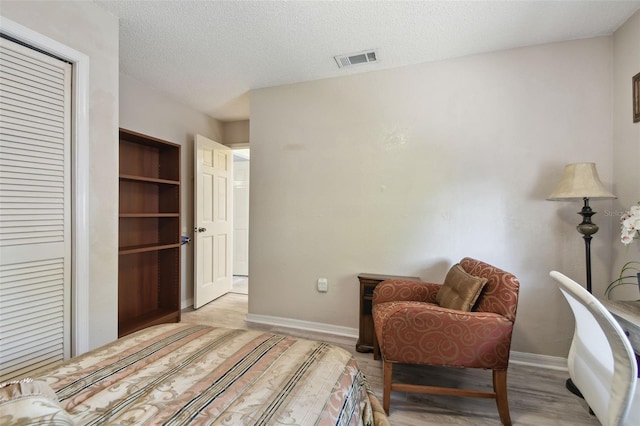 sitting room with a textured ceiling, visible vents, light wood finished floors, and baseboards