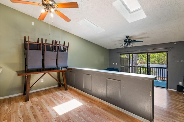 interior space featuring a textured ceiling, ceiling fan, wood finished floors, and lofted ceiling with skylight
