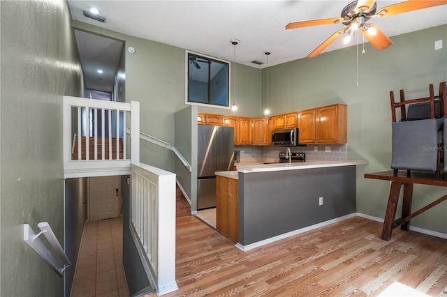 kitchen featuring a ceiling fan, tasteful backsplash, a peninsula, stainless steel appliances, and light wood-style floors