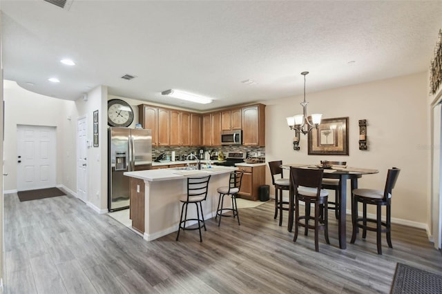 kitchen with light countertops, appliances with stainless steel finishes, an island with sink, light wood-style floors, and backsplash