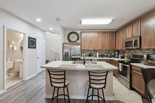 kitchen featuring decorative backsplash, visible vents, appliances with stainless steel finishes, a sink, and a breakfast bar area