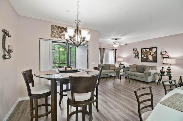 dining space with baseboards, wood finished floors, and ceiling fan with notable chandelier