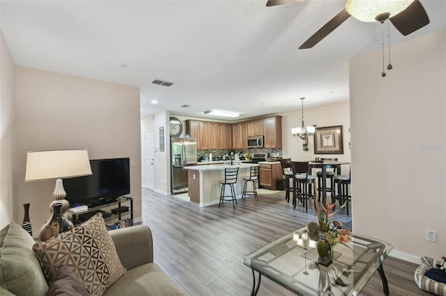 living room with light wood-style flooring, ceiling fan with notable chandelier, baseboards, and visible vents