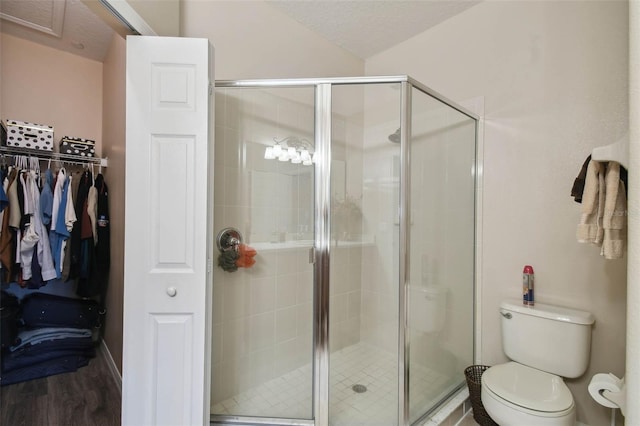 bathroom with a spacious closet, toilet, a stall shower, and wood finished floors