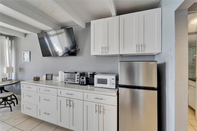 kitchen with white cabinets, freestanding refrigerator, beam ceiling, white microwave, and light tile patterned flooring