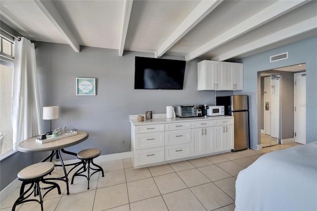 kitchen featuring white microwave, freestanding refrigerator, beamed ceiling, white cabinetry, and visible vents