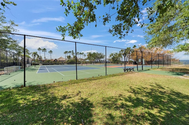view of tennis court featuring fence and a lawn