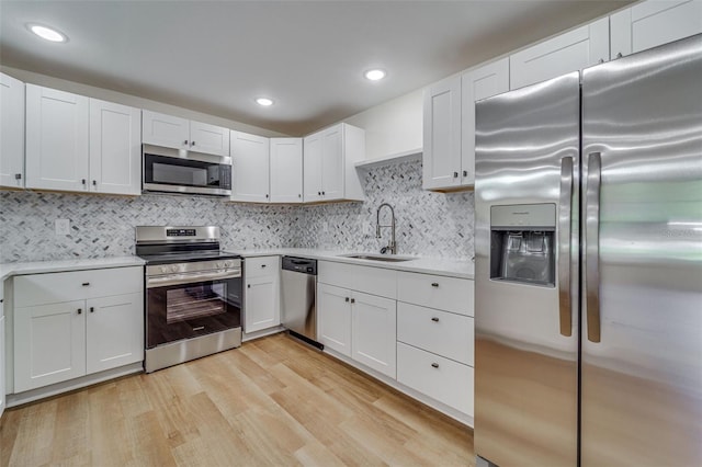kitchen featuring light countertops, a sink, light wood finished floors, white cabinetry, and appliances with stainless steel finishes