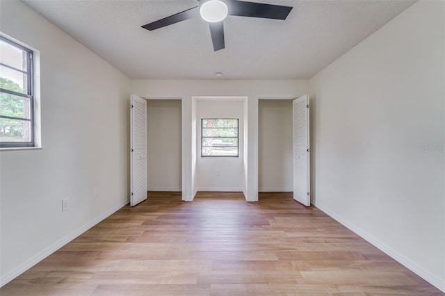 unfurnished bedroom featuring a textured ceiling, multiple closets, light wood-type flooring, baseboards, and ceiling fan