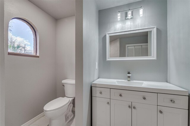 half bath featuring baseboards, toilet, and vanity