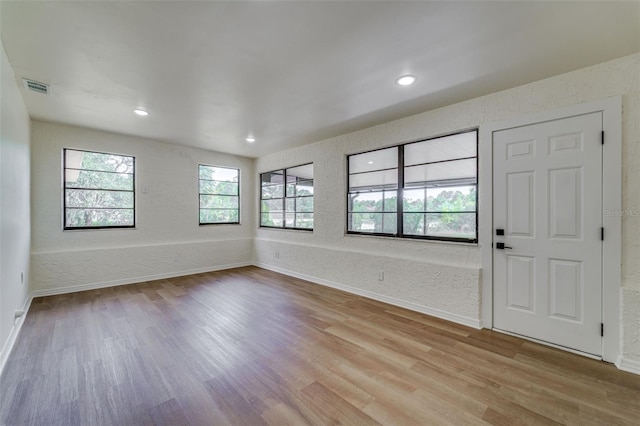 entrance foyer featuring baseboards, visible vents, a textured wall, and light wood-type flooring
