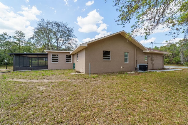 rear view of property with stucco siding, a sunroom, central AC unit, and a yard