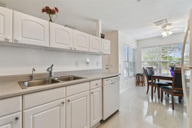 kitchen with white appliances, a textured ceiling, white cabinets, light countertops, and a sink
