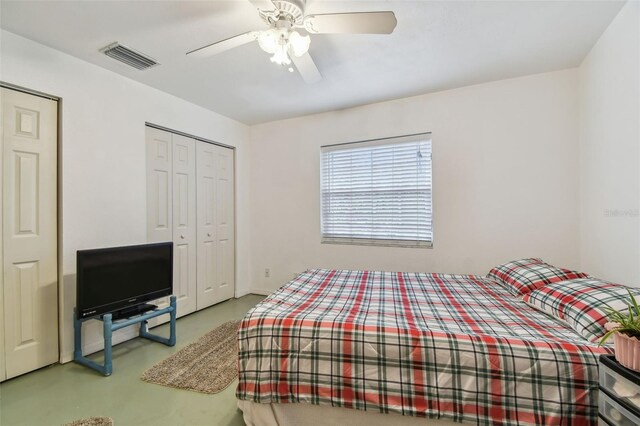 bedroom featuring concrete floors, visible vents, a ceiling fan, and two closets