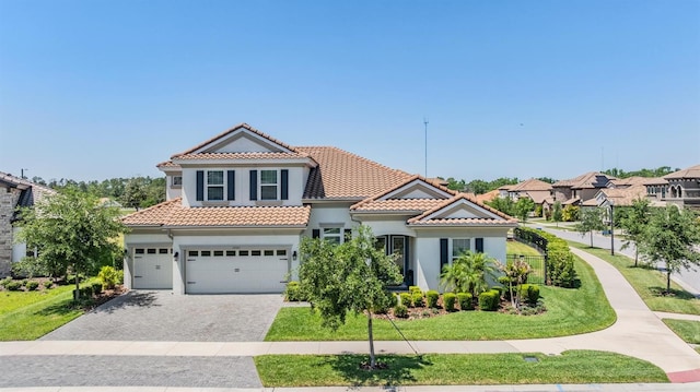 mediterranean / spanish-style home featuring a tile roof, decorative driveway, an attached garage, a front yard, and stucco siding