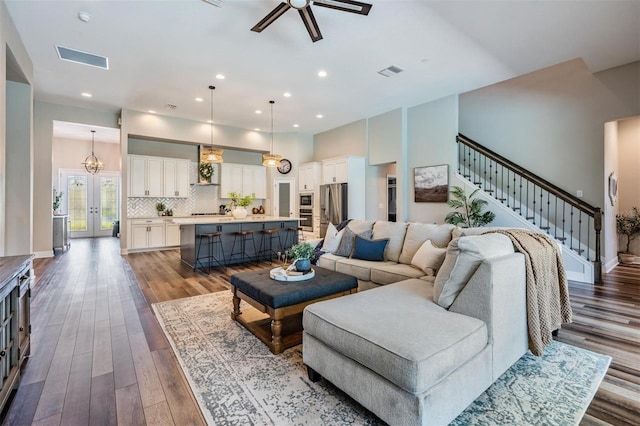 living area with a ceiling fan, visible vents, stairway, and dark wood-style flooring