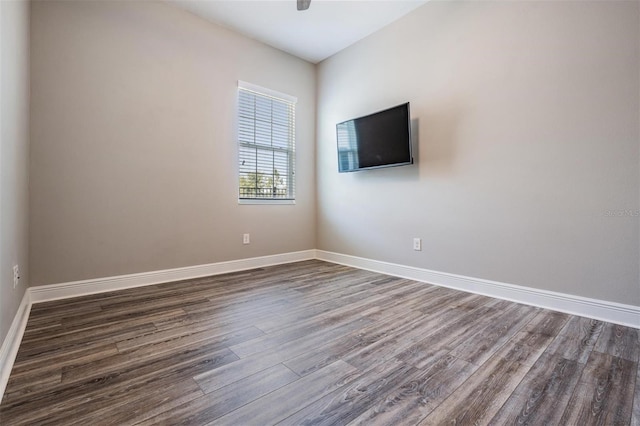 spare room with baseboards and dark wood-type flooring