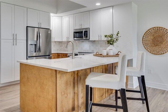 331 Cleveland St Unit 320, Clearwater, FL 33755 - kitchen with decorative backsplash, white cabinets, light wood-style flooring, appliances with stainless steel finishes, and light stone counters