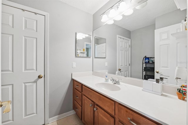 bathroom with baseboards, tile patterned flooring, vanity, and a textured ceiling