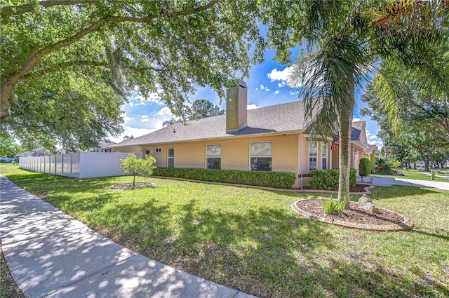 ranch-style house with a front yard, a shingled roof, a chimney, fence, and stucco siding
