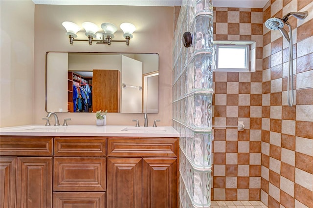bathroom featuring double vanity, a tile shower, and a sink