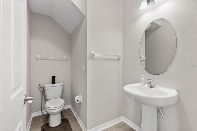 half bathroom with toilet, wood finished floors, baseboards, and lofted ceiling