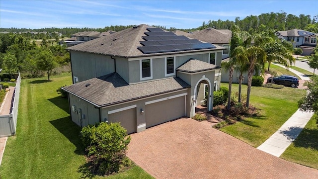 view of front of home with a front yard, a shingled roof, solar panels, stucco siding, and decorative driveway