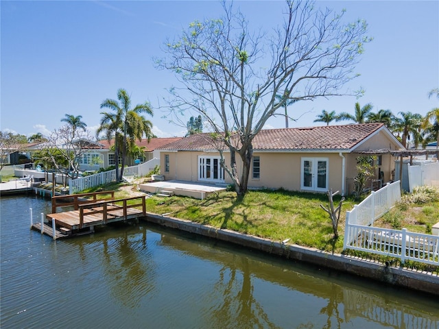 back of house featuring french doors, stucco siding, a fenced backyard, a lawn, and a water view