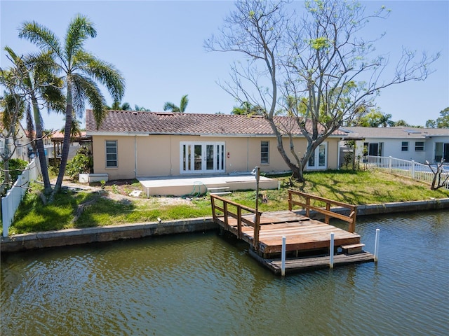 rear view of house featuring french doors, a water view, stucco siding, and a lawn