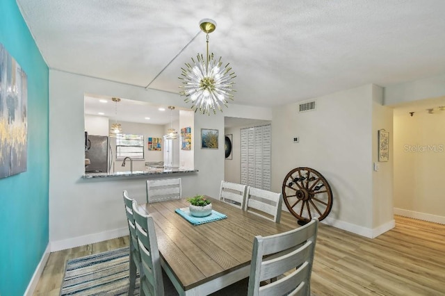 dining space with a chandelier, wood finished floors, baseboards, and visible vents