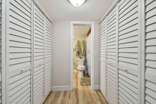 corridor featuring baseboards, light wood-type flooring, and a textured ceiling