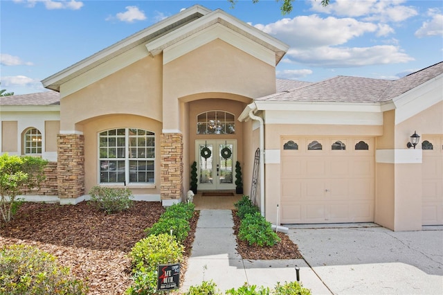 property entrance featuring stucco siding, roof with shingles, an attached garage, french doors, and driveway