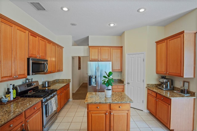 kitchen with a kitchen island, light tile patterned flooring, stone countertops, visible vents, and appliances with stainless steel finishes