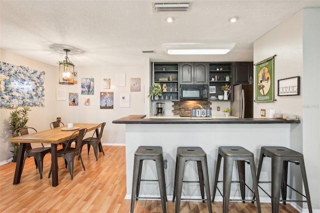9481 Highland Oak Dr Unit 1616, Tampa, FL 33647 - bar area with black microwave, freestanding refrigerator, a textured ceiling, light wood-type flooring, and baseboards