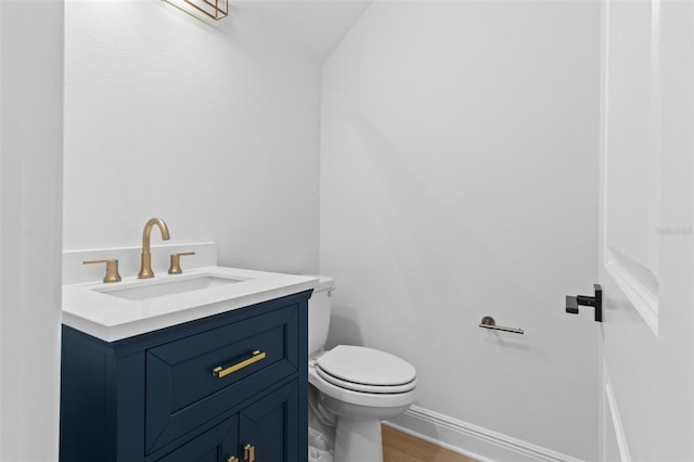 half bathroom featuring vanity, toilet, wood finished floors, and baseboards