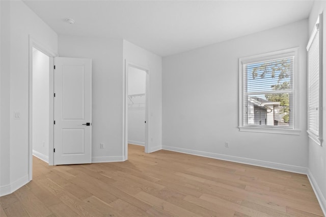 unfurnished bedroom with light wood-style floors, a walk in closet, baseboards, and a closet