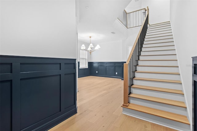 stairway featuring a chandelier, wood finished floors, a wainscoted wall, and a decorative wall