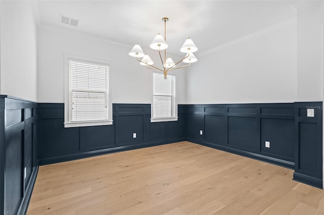 unfurnished dining area featuring wainscoting, ornamental molding, a chandelier, light wood-style floors, and a decorative wall