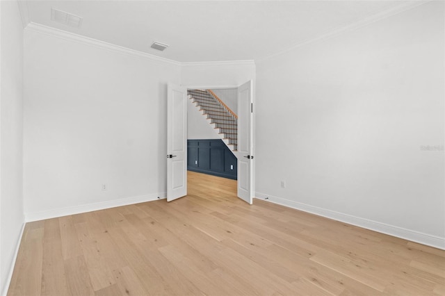 spare room with crown molding, light wood-style floors, baseboards, and stairway