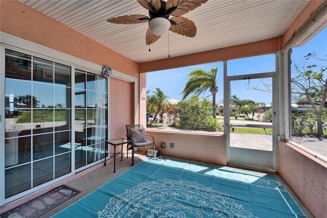 sunroom / solarium with ceiling fan, a textured wall, and carpet