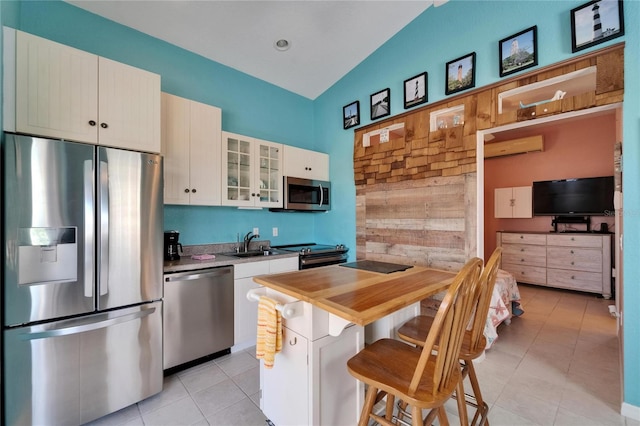 kitchen with white cabinets, a kitchen breakfast bar, light tile patterned floors, glass insert cabinets, and appliances with stainless steel finishes